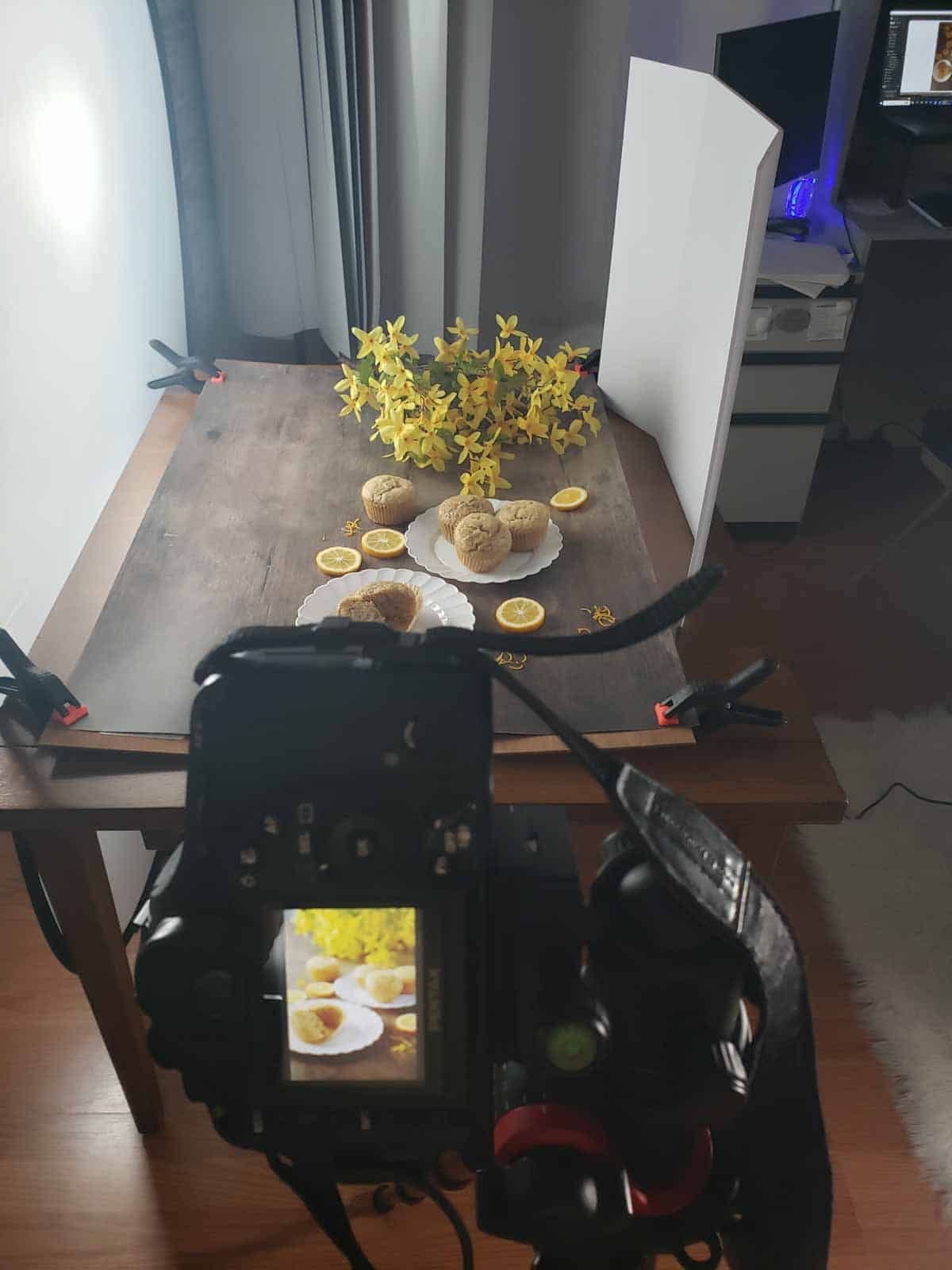 Scene set up for recipe photoshoot and the camera showing the last shot taken of the food displayed on a dark wood backdrop with lemons for decoration.