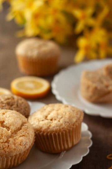 Three muffins on a white decorative plate with yellow flowers in the background and lemon slices for decoration.