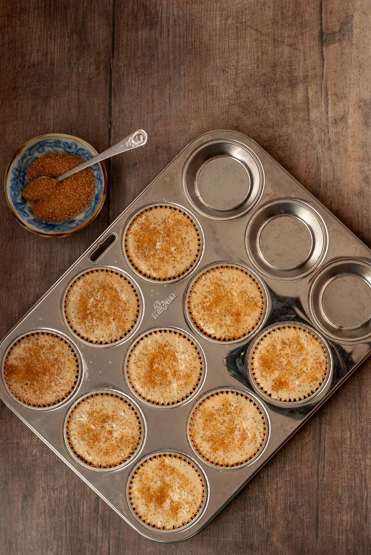 Muffin tin filled with batter along side a bowl of coconut sugar.