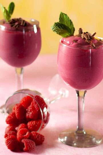 Raspberry pudding in tall glasses with chocolate curls and mint leaves.