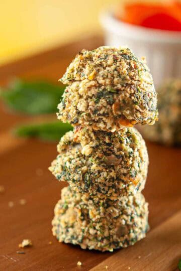 Three spinach balls stacked on a wooden cutting board.