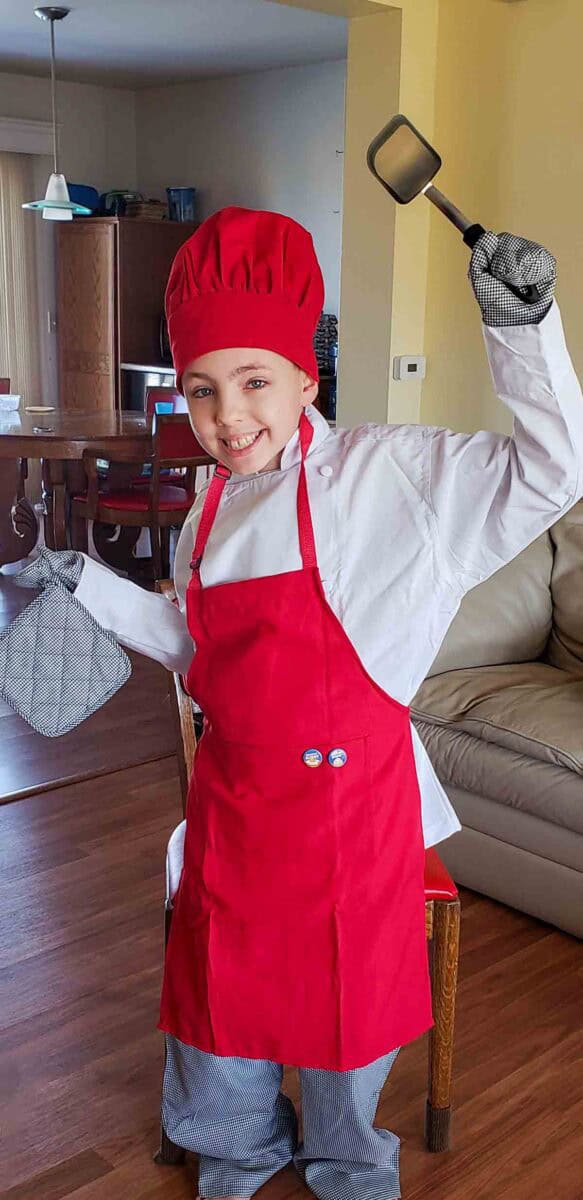 Justin in his red apron holding a spatula and an oven mit.