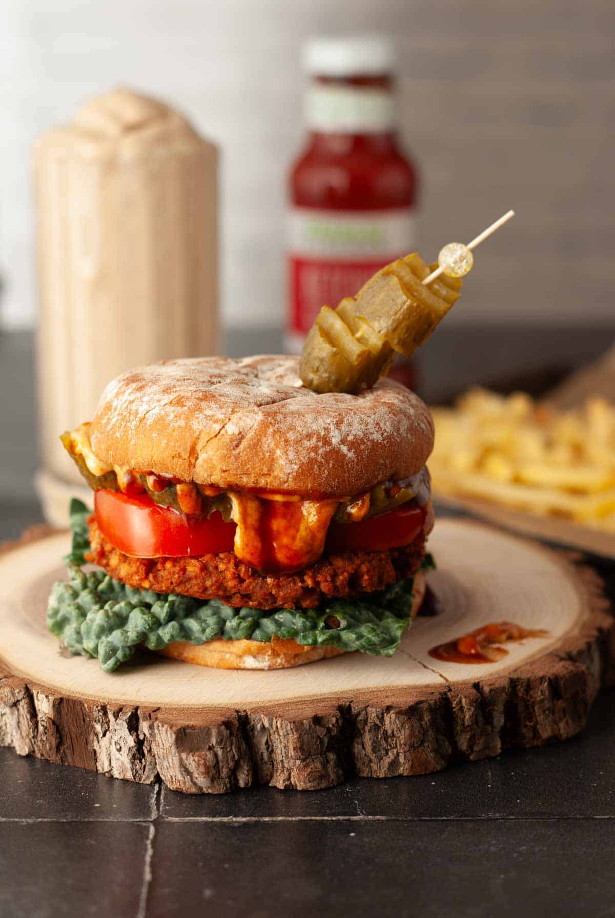 Baked vegan TVP and lentil burger on a bun with kale, pickles, sauce, and tomato.
