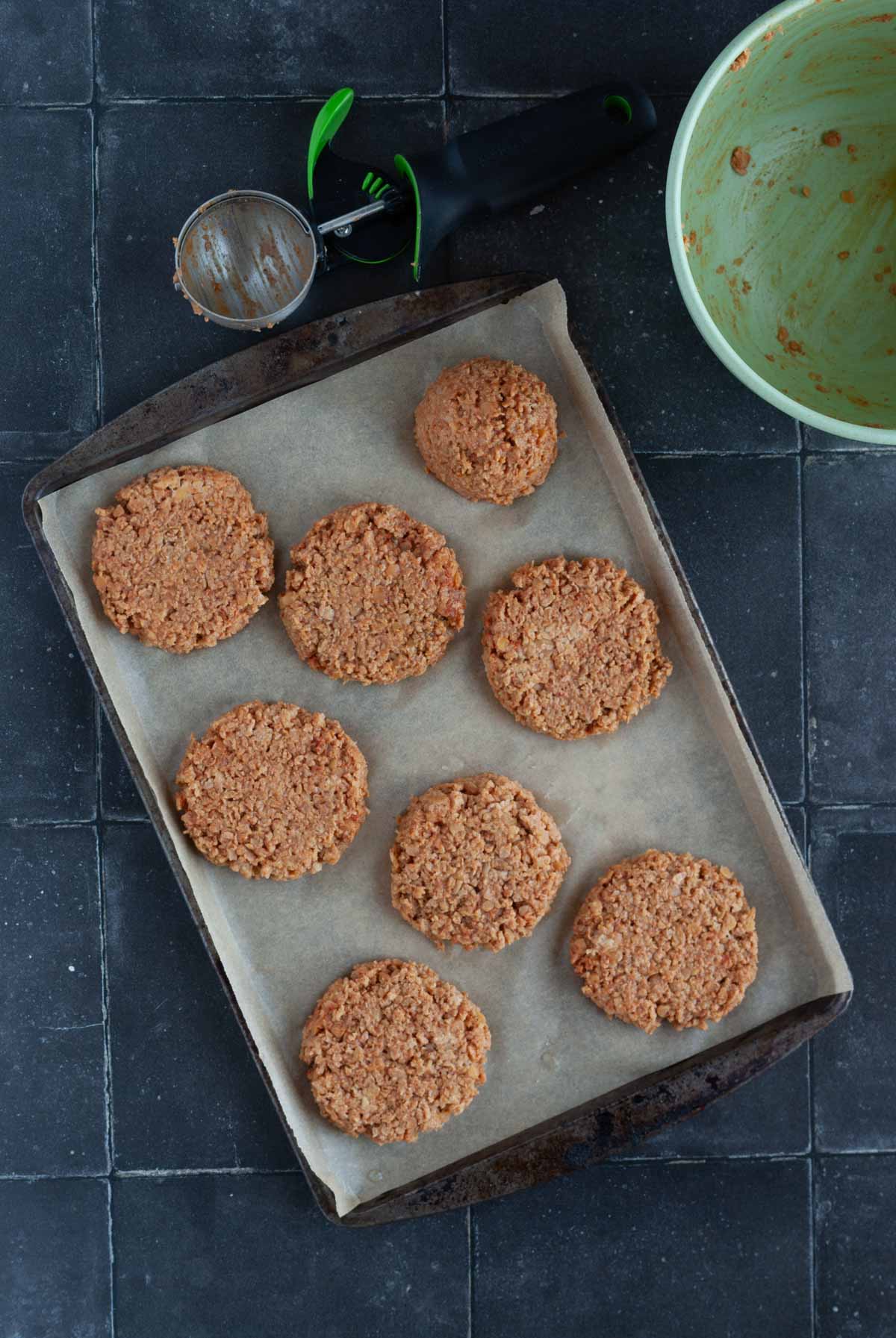 TVP and lentil burger patties on a baking sheet next to an empty scoop and mixing bowl.