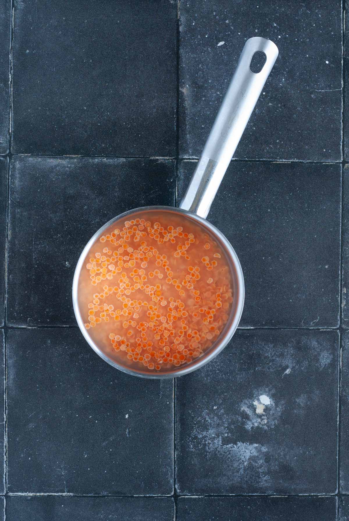 Red lentils simmering in a pan of water.