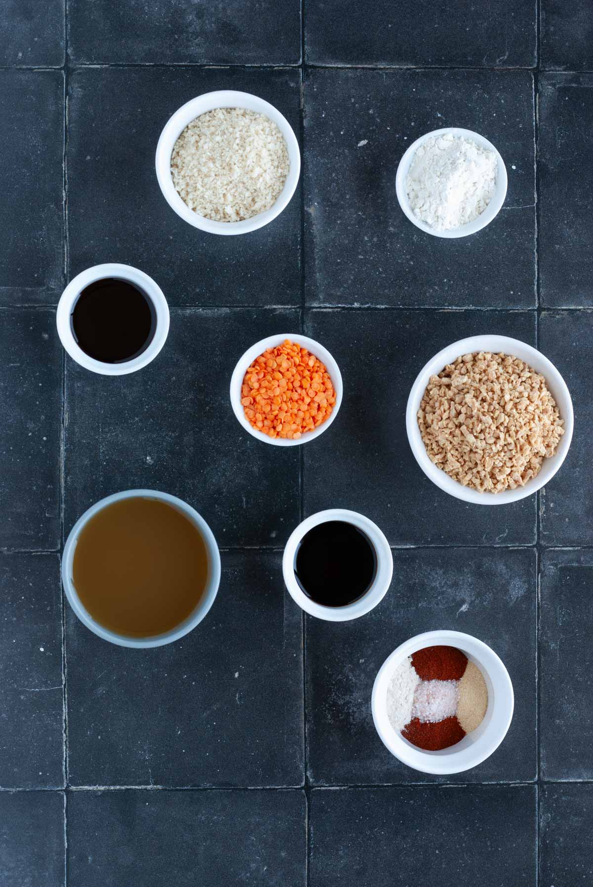 Ingredients for vegan TVP lentil burgers including dry lentils, TVP, spices, broth, and breadcrumbs in small individual bowls.