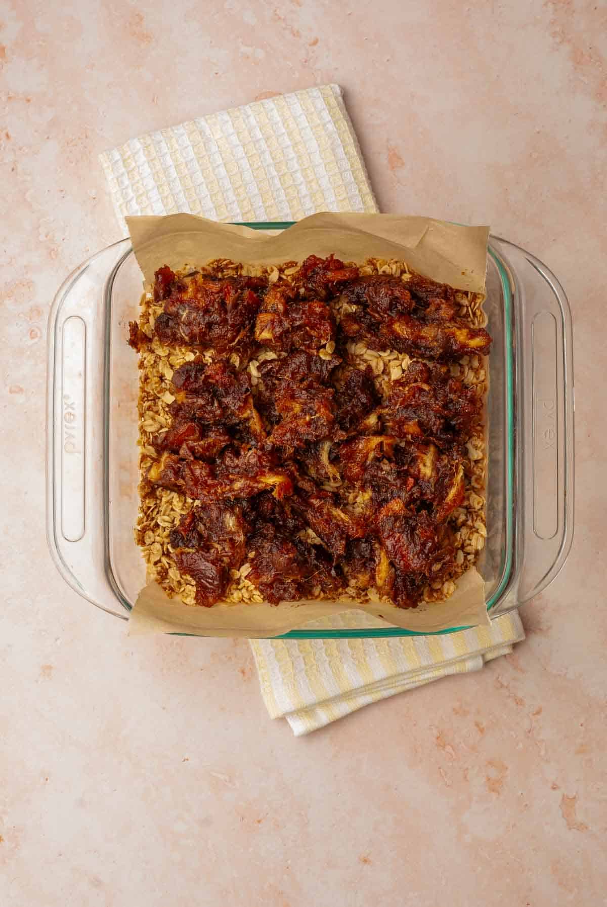 Spoonfuls of softened medjool dates over a baked oat crust in a baking dish ready for spreading.