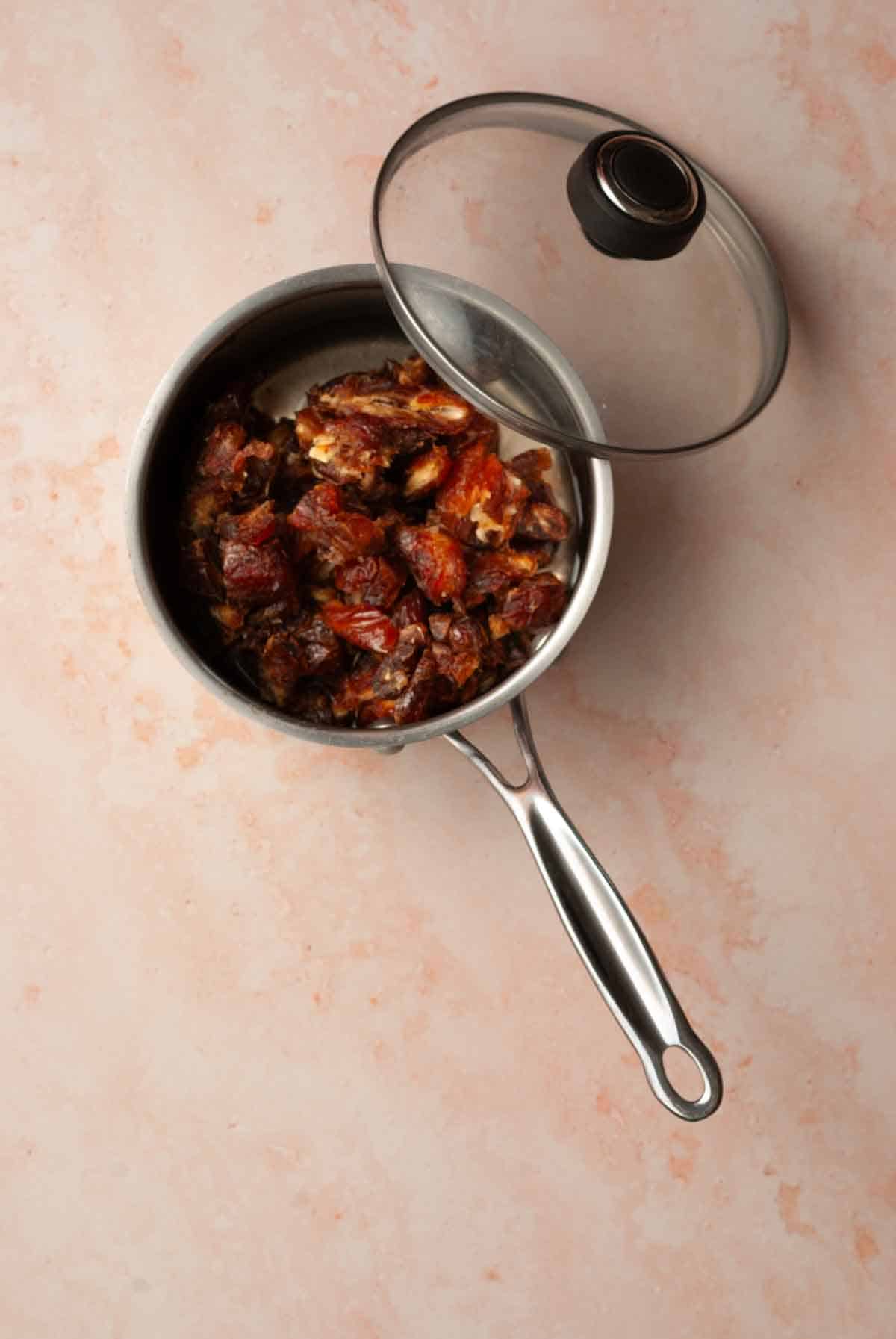 A sauce pan filled with chopped medjool dates, water and baking soda with a lid next tot he pan.