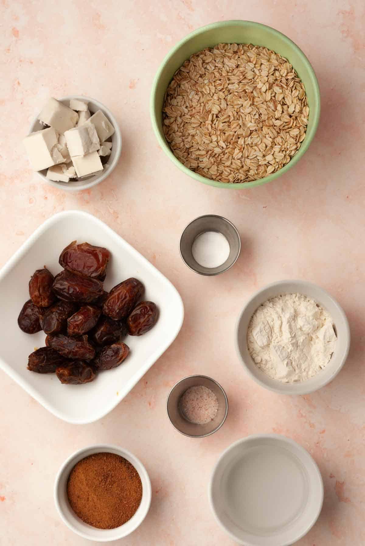 Ingredients for making vegan date bars shown in separate bowls including oats, dates, and coconut sugar.