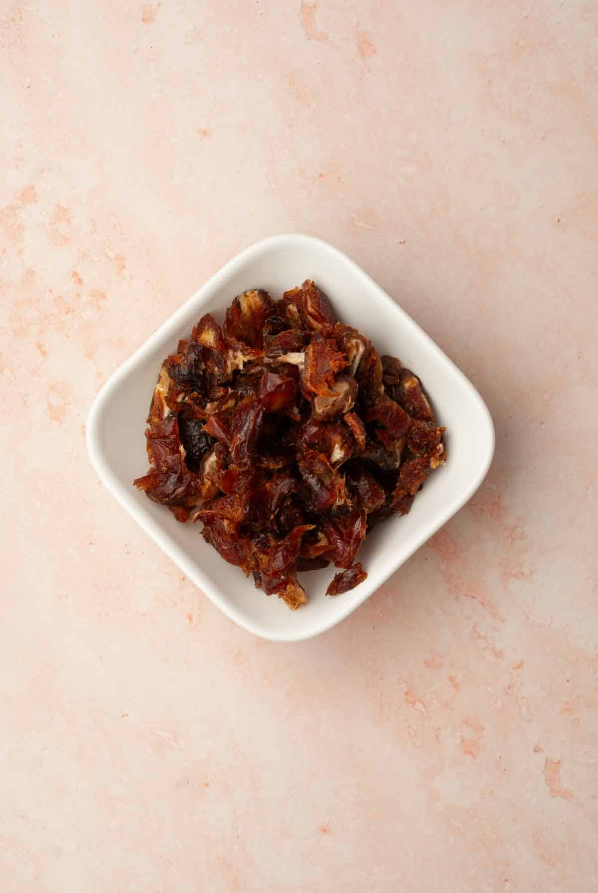 A white square bowl filled with chopped medjool dates.