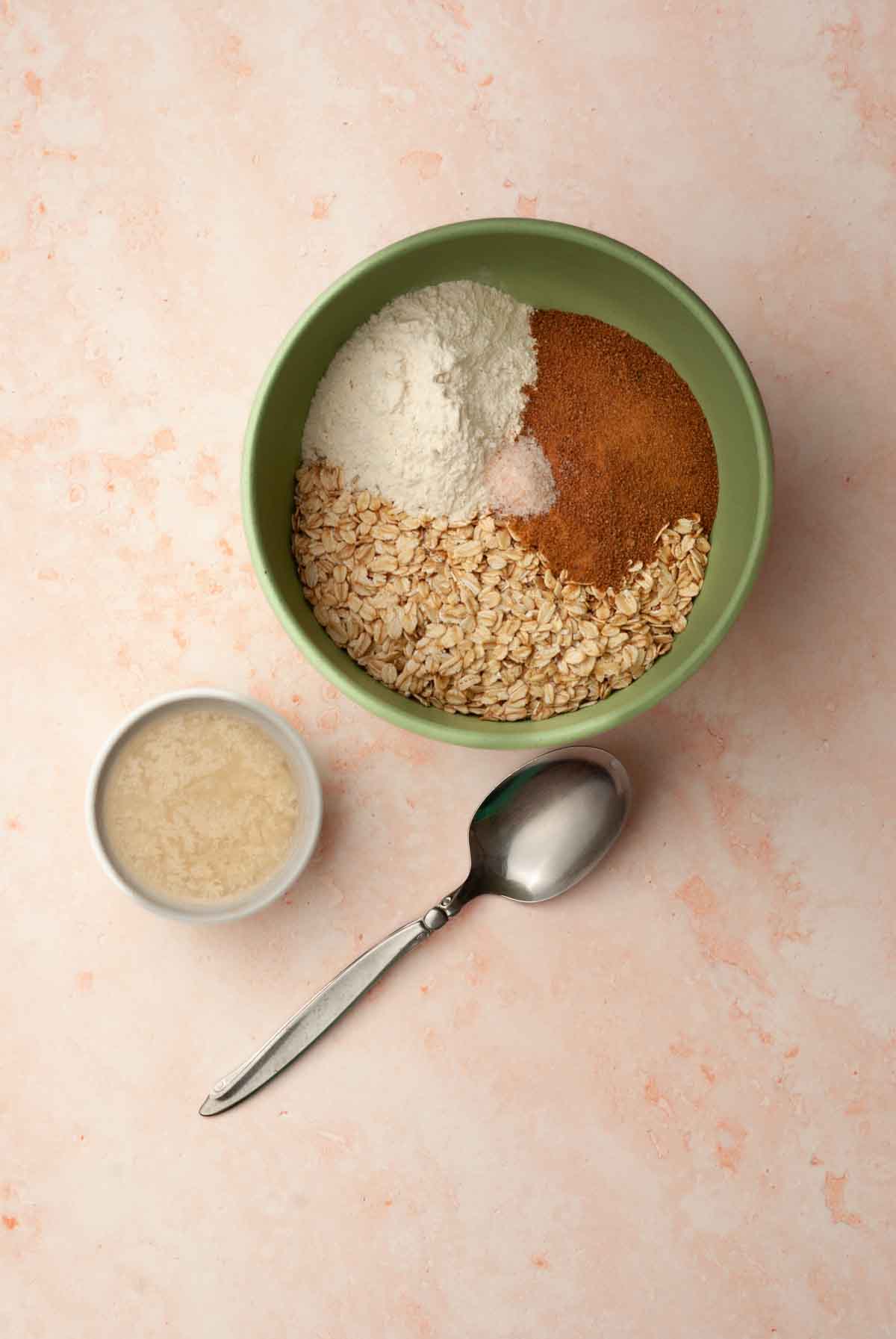 A small bowl of melted vegan butter next to a mixing bowl filled with oats, flour, coconut sugar and salt.
