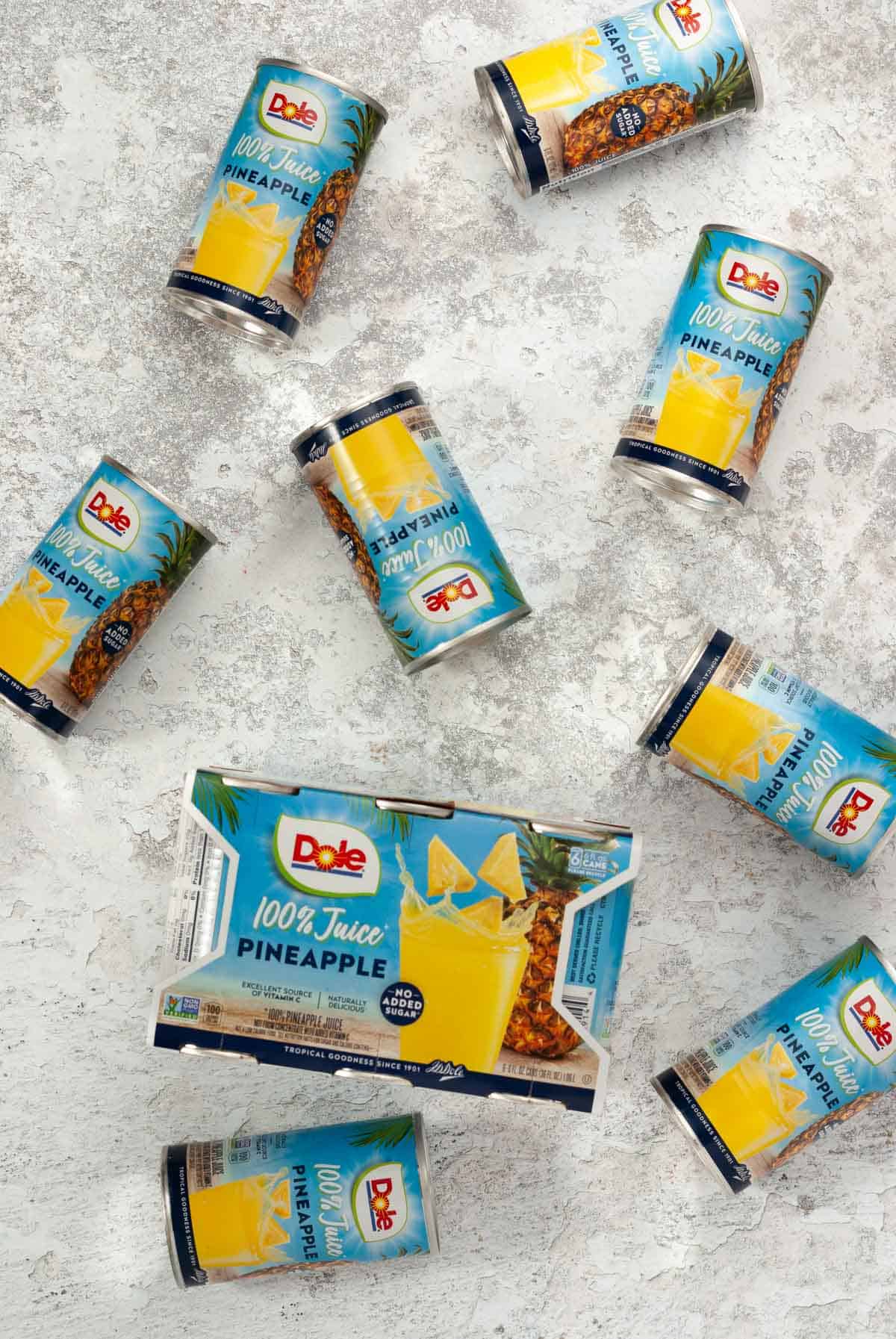 Several small cans of Dole Pineapple juice laying all over a countertop for display.