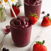 Dark red mixed berry smoothie on a white wood table with strawberries, blueberries and daisies in the background.