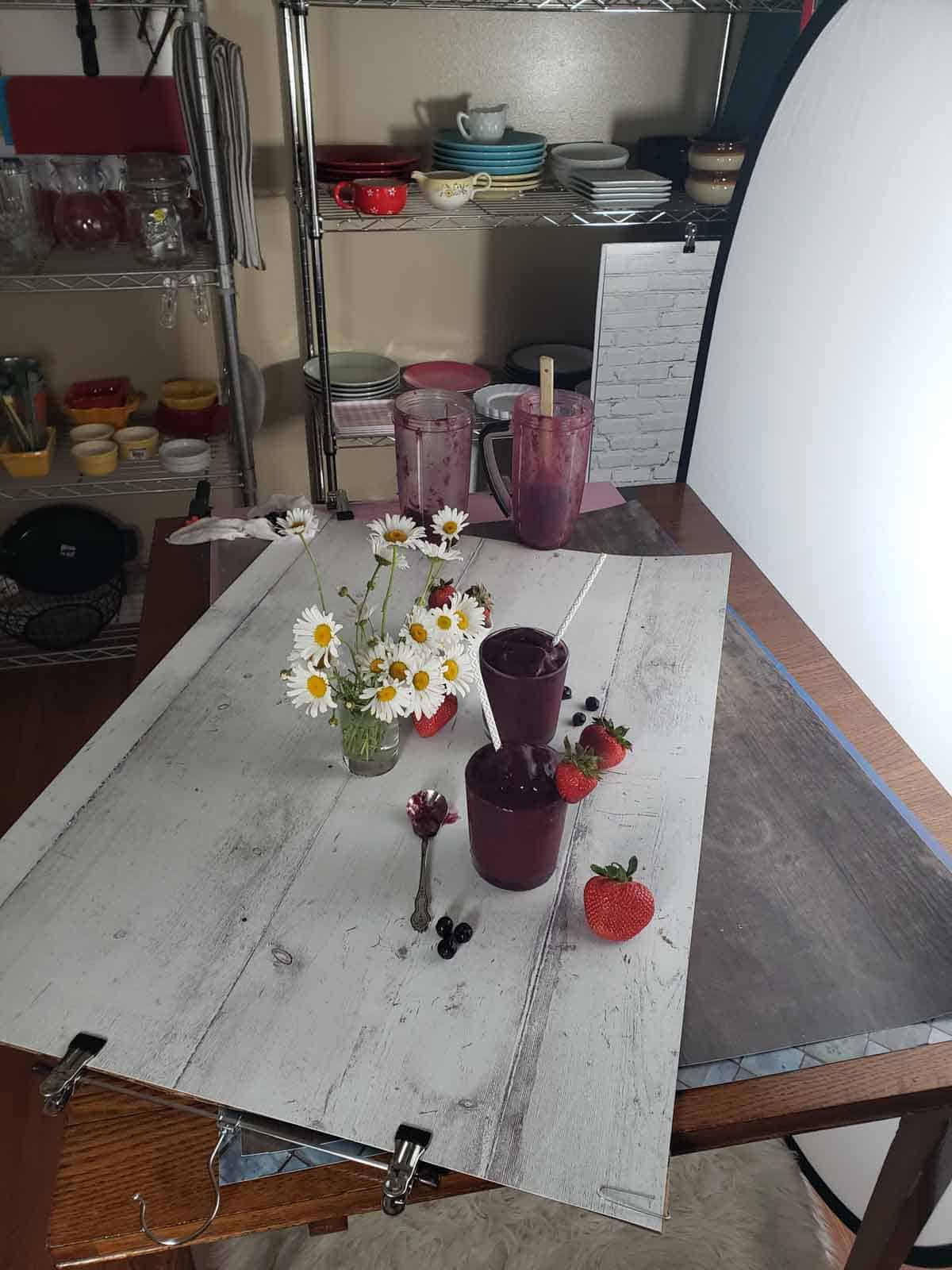 The smoothies set up on a backdrop with daisies and fresh strawberries and blueberries.