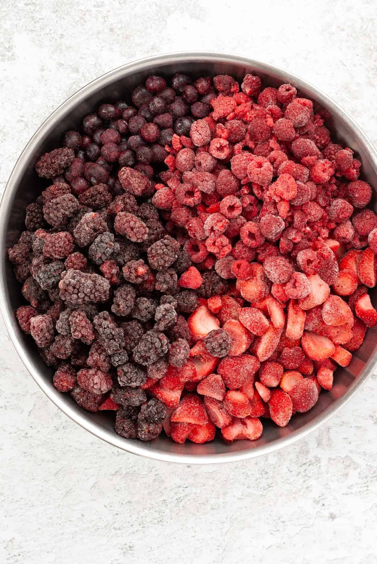 A large bow of frozen berries on a counter top including raspberries, blueberries, strawberries, and blackberries for a mixed berry smoothie recipe.