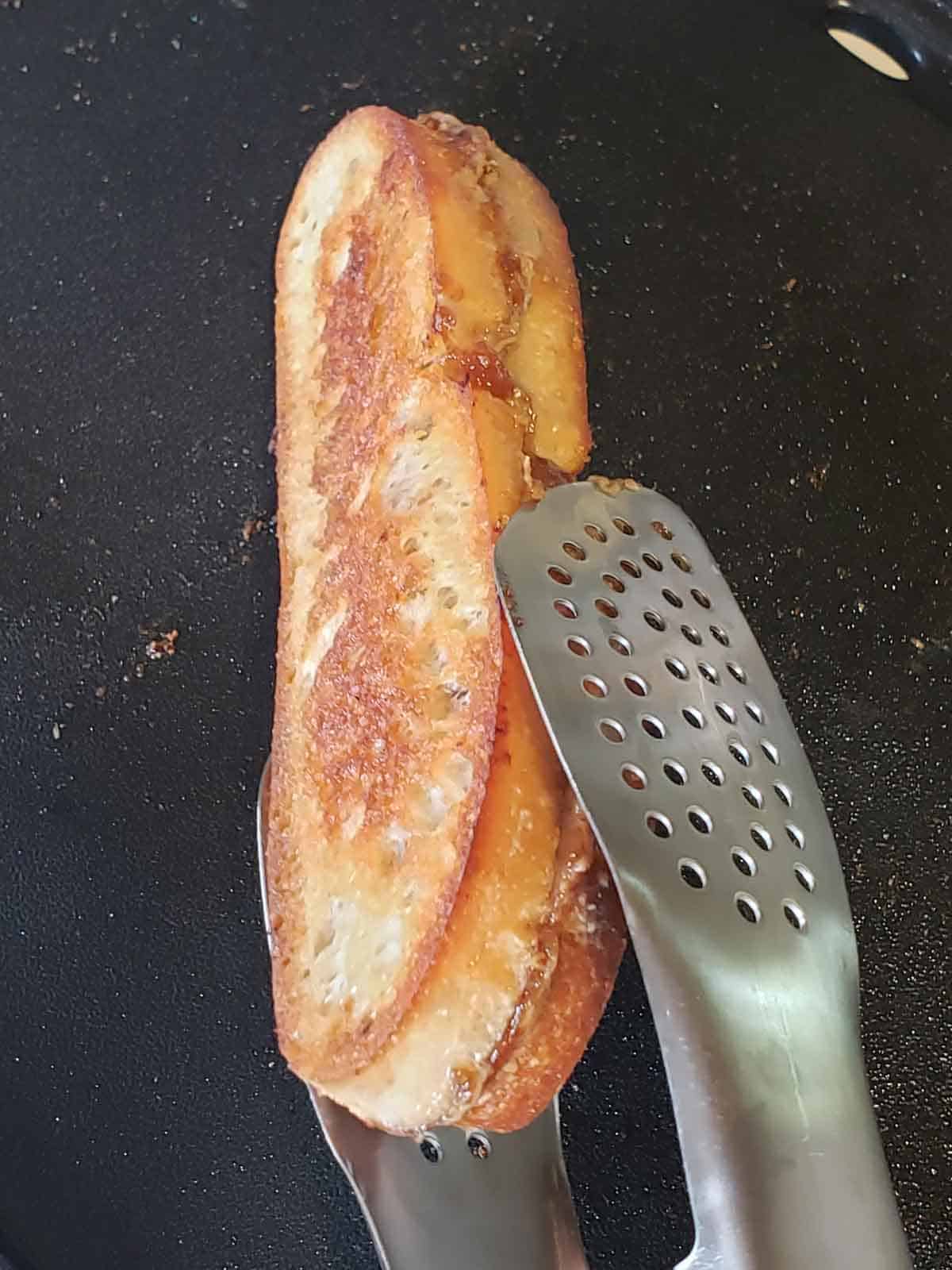 A pair of tongs flipping a sunbutter sandwich on a griddle.