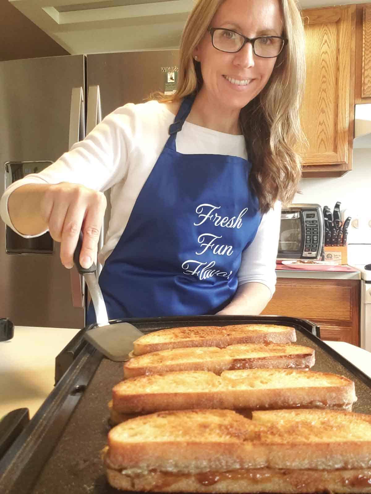 Rhonda wearing a blue apron in the kitchen grilling the sunbutter sandwiches on a griddle.