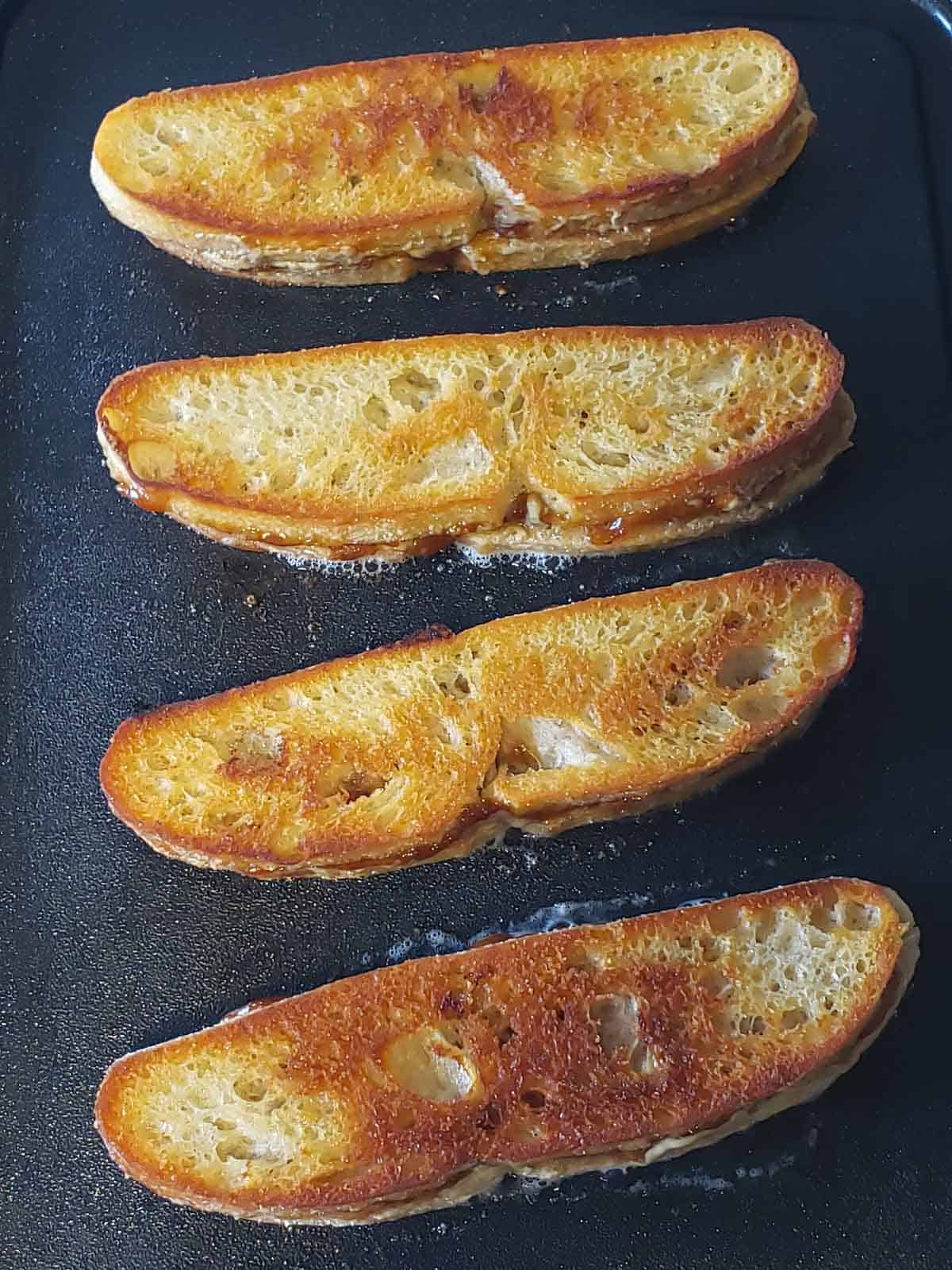 4 golden brown sunbutter & jelly sandwiches in the finishing stages of grilling on a griddle.