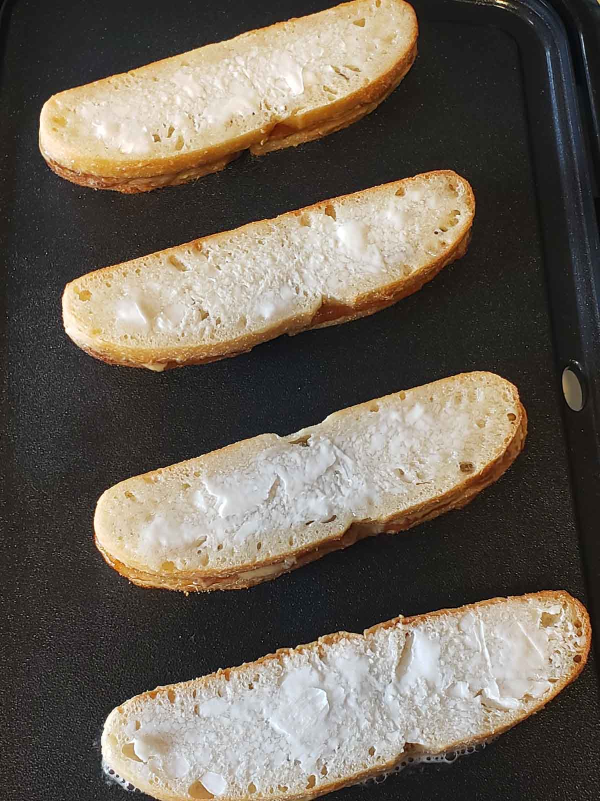 4 buttered sunbutter & jelly sandwich sticks cooking on a griddle.