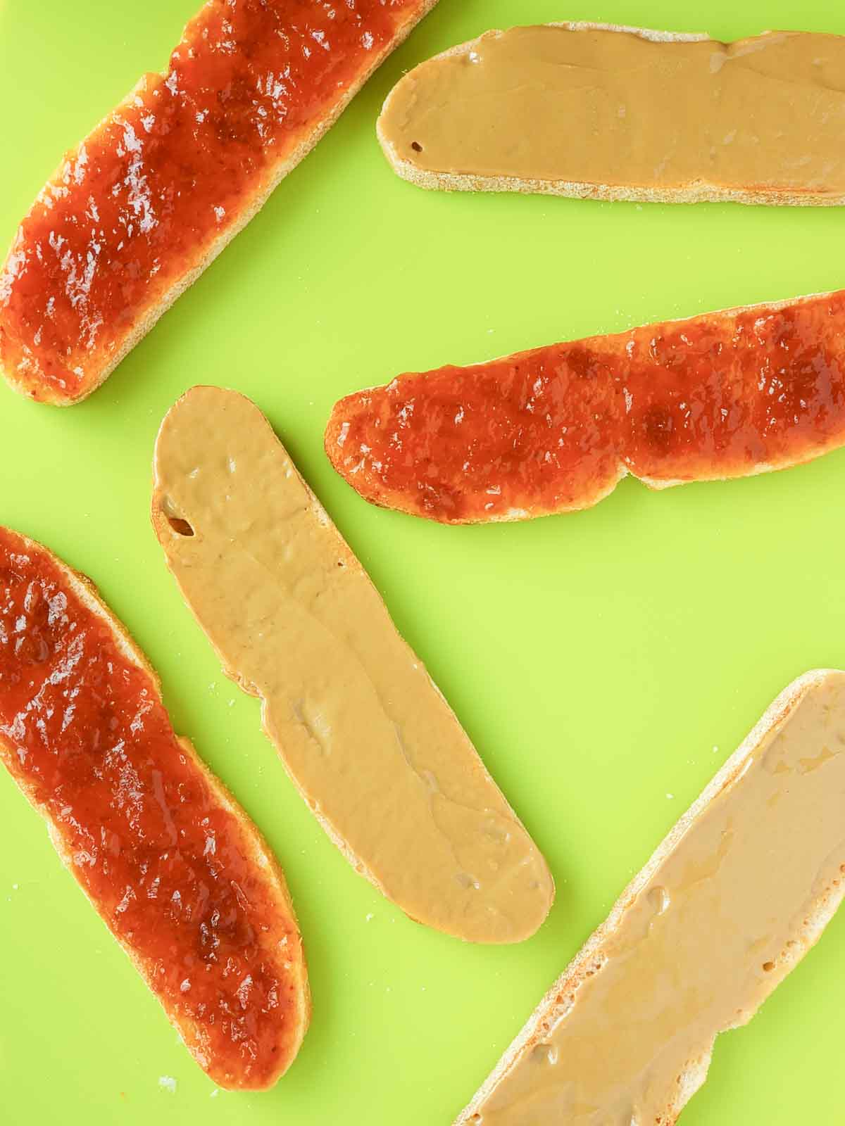 6 Bread slices shown on a cutting board with half spread with sunbutter and half spread with strawberry jelly.