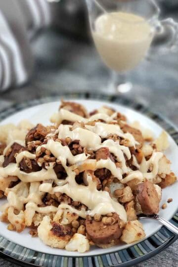 Vegan sausage and lentils with balsamic reduction on a plate of roasted cauliflower and drizzled with the lemon tahini sauce.