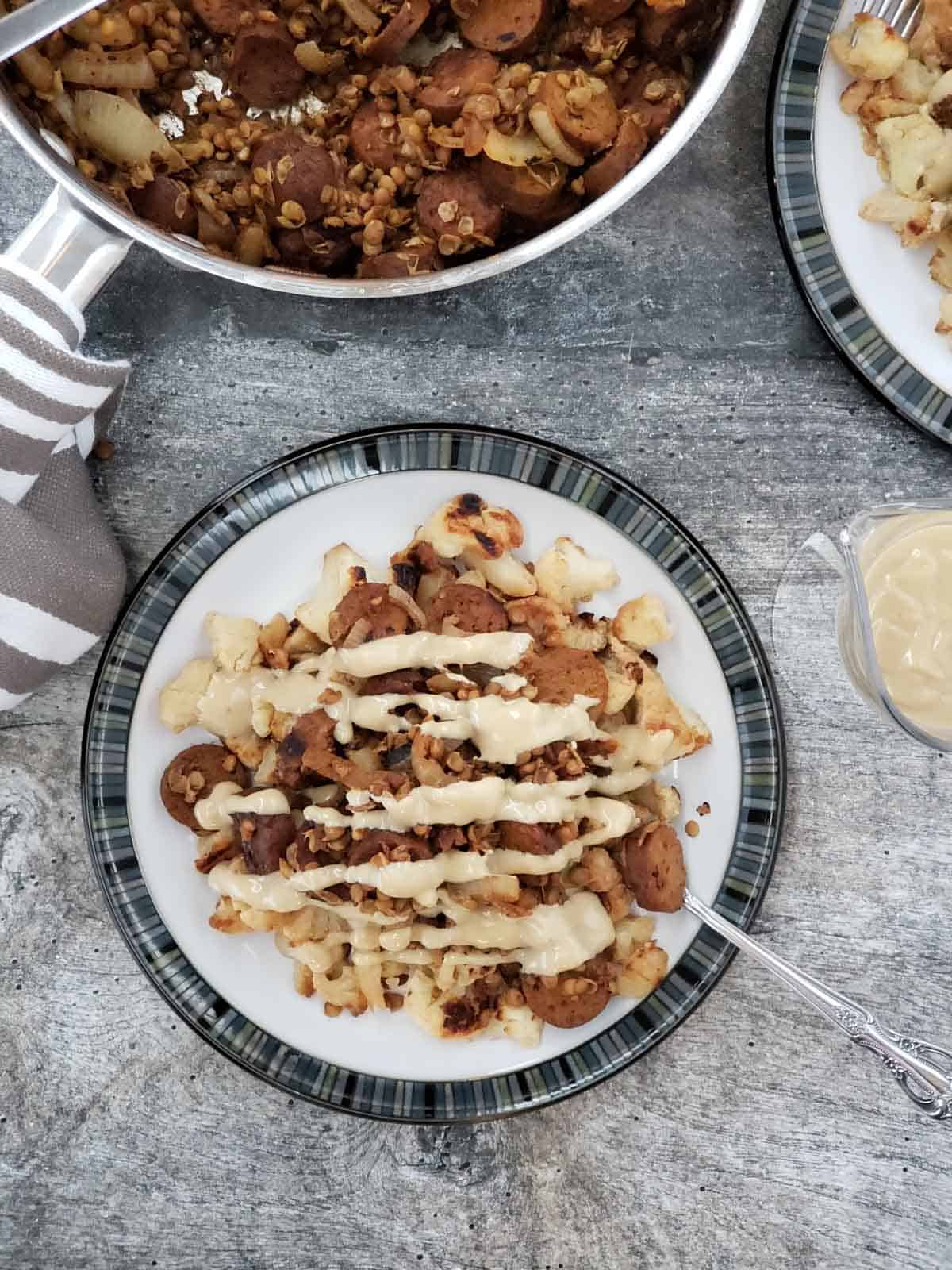 Vegan sausage and lentils with balsamic reduction on a plate of roasted cauliflower and drizzled with the lemon tahini sauce.