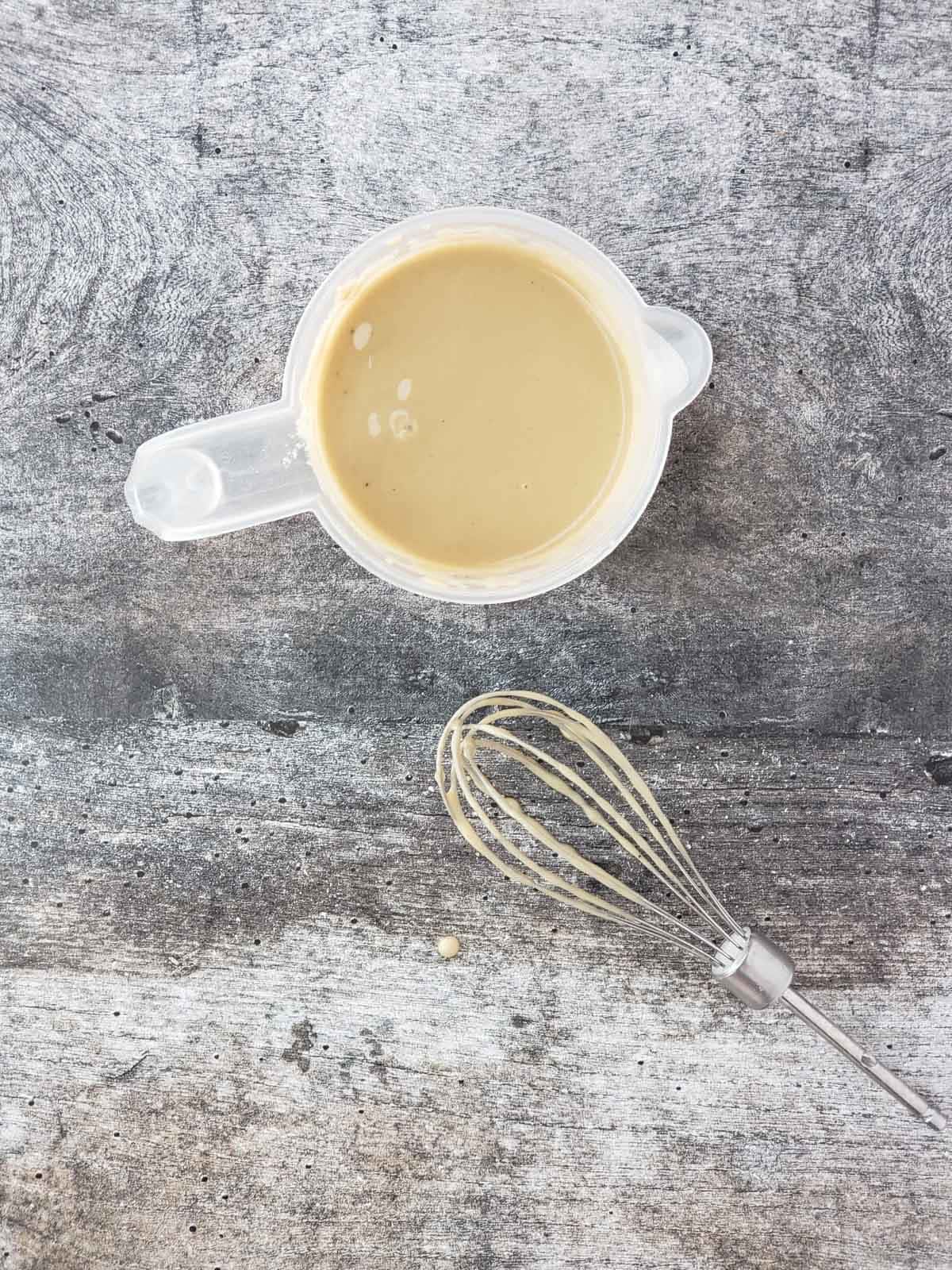A cup of lemon tahini sauce and a whisk shown next to it.