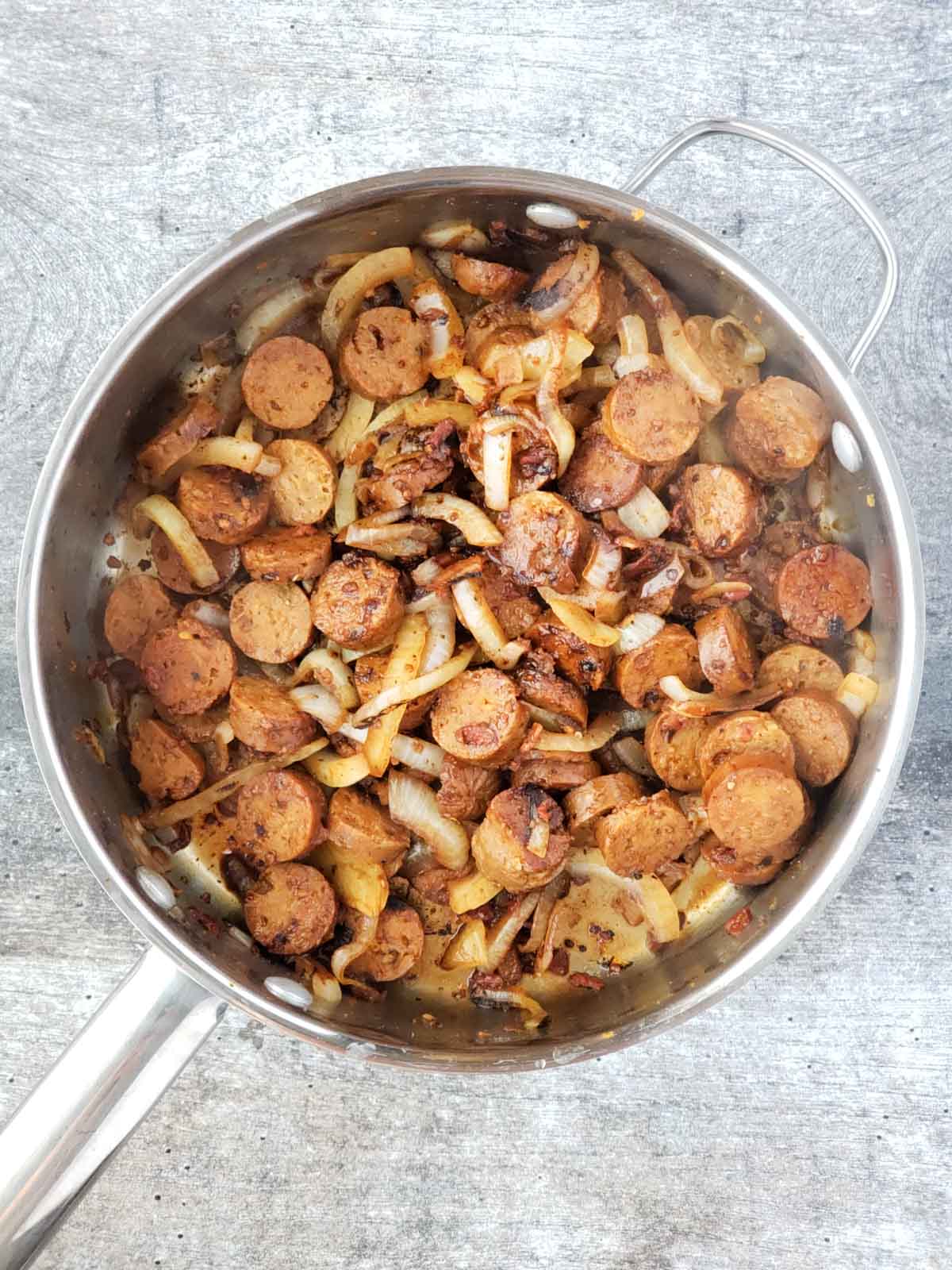 A pan of cooked vegan sausage and sliced caramelized onions.