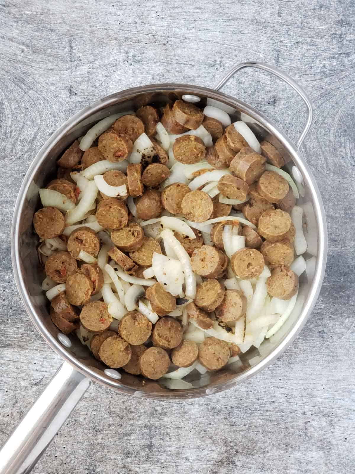 A pan of sliced vegan sausage and sliced onions being prepared for the roasted cauliflower recipe.