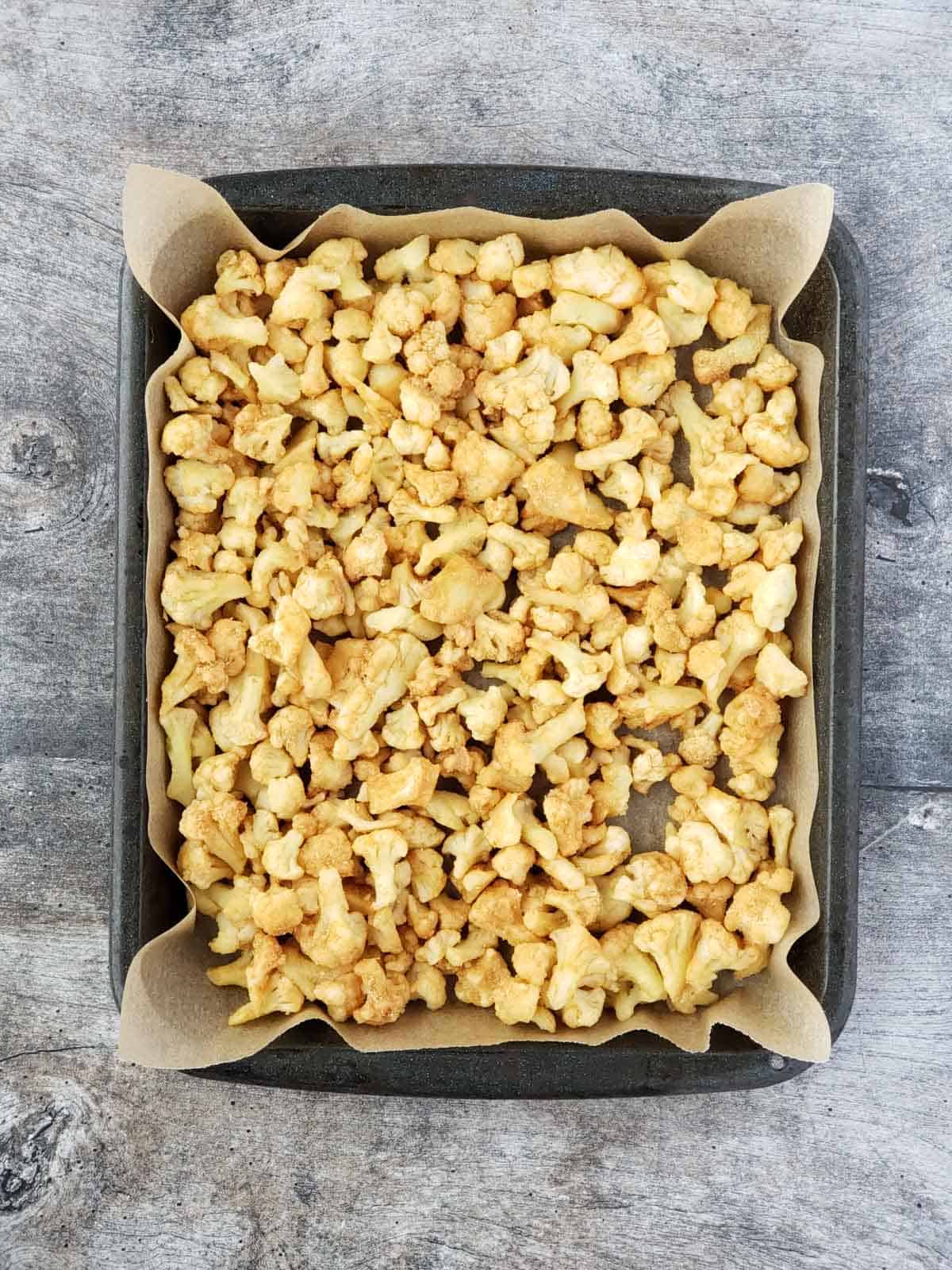 A pan lined with parchment paper and filled with seasoned cauliflower for raosting.