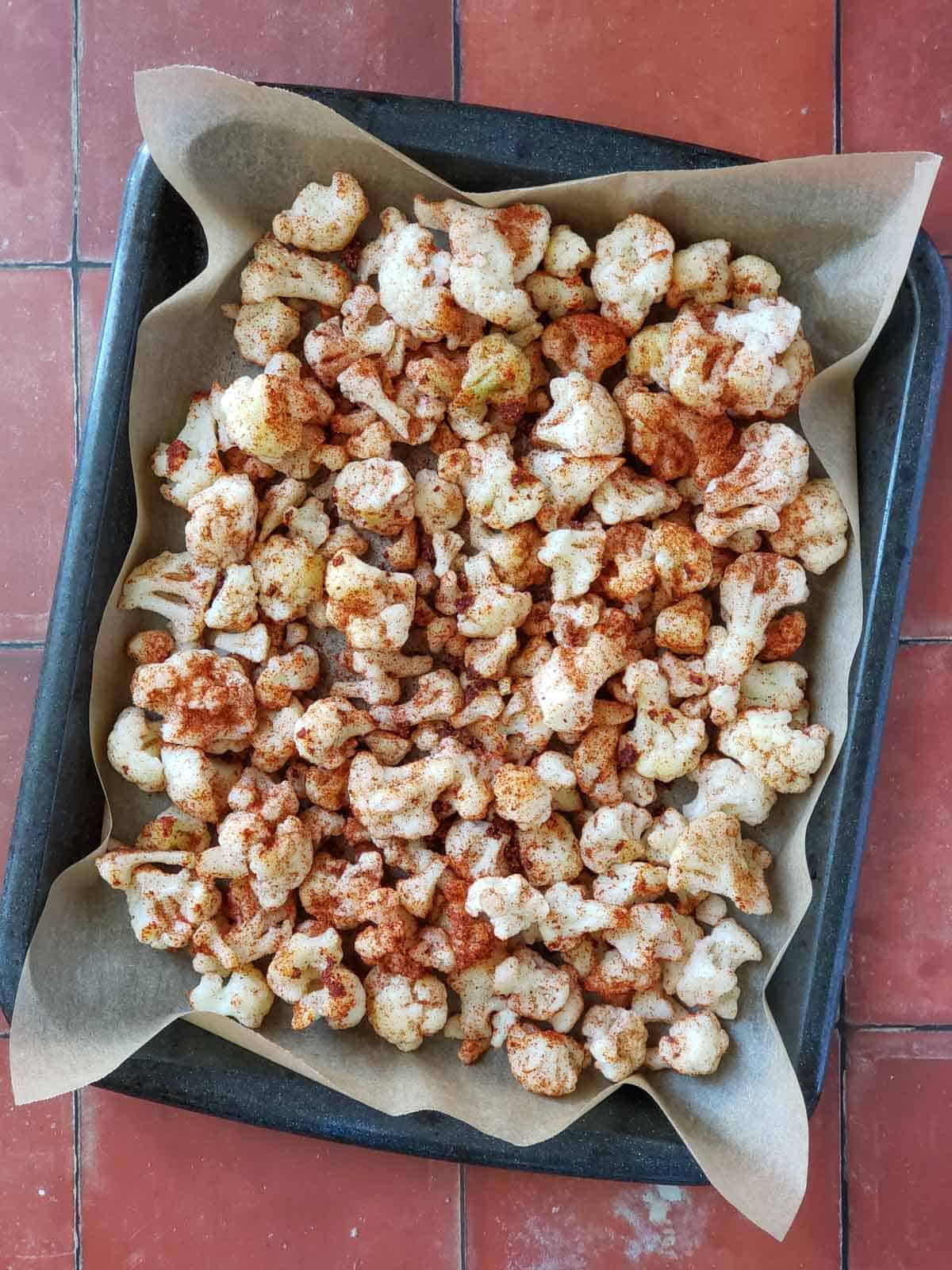 A baking tray of frozen cauliflower florets seasoned with bbq seasoning.