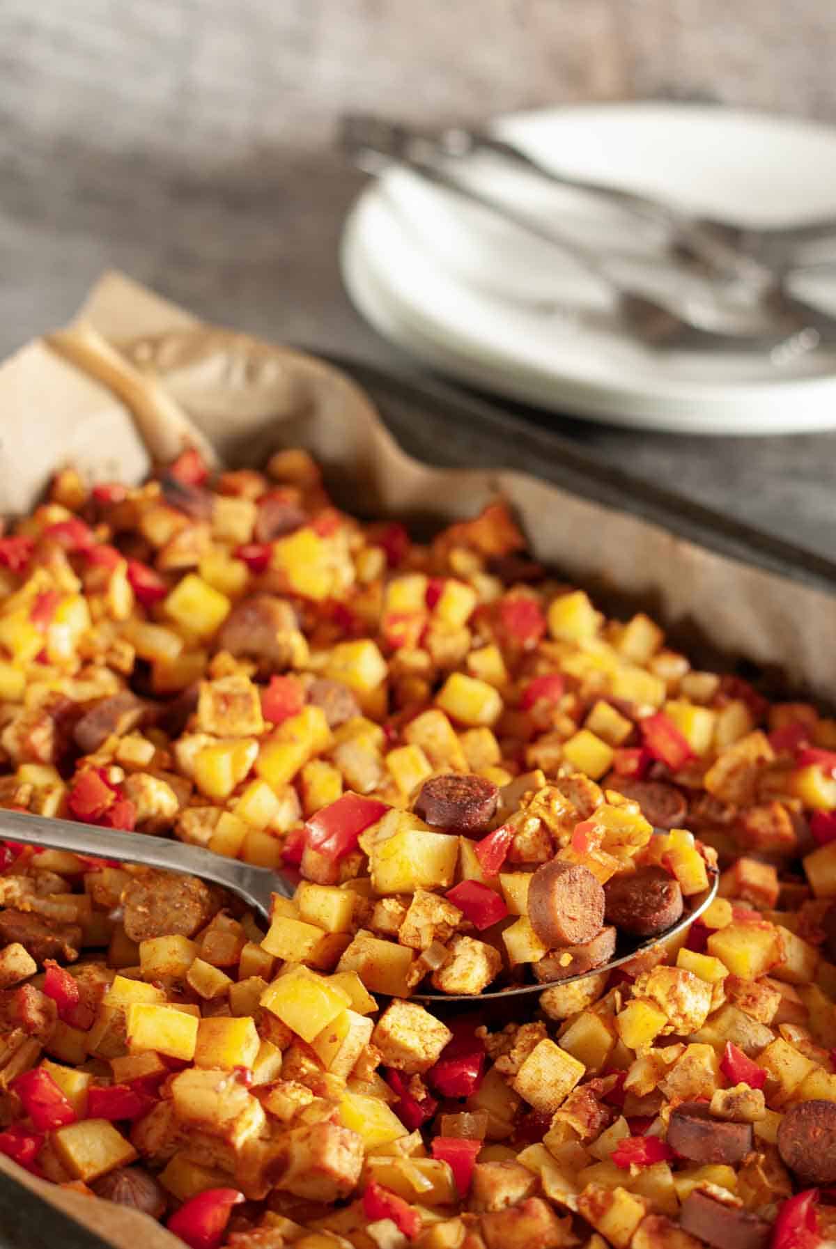 Close up of vegan breakfast hash being served up with a spoon, and white plates with forks in the background.