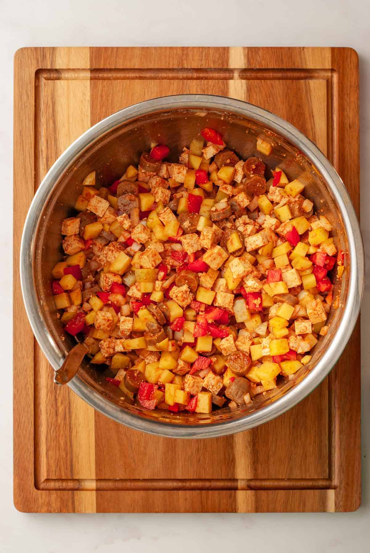 Mixing ingredients for the breakfast hash in a large mixing bowl with a spoon.