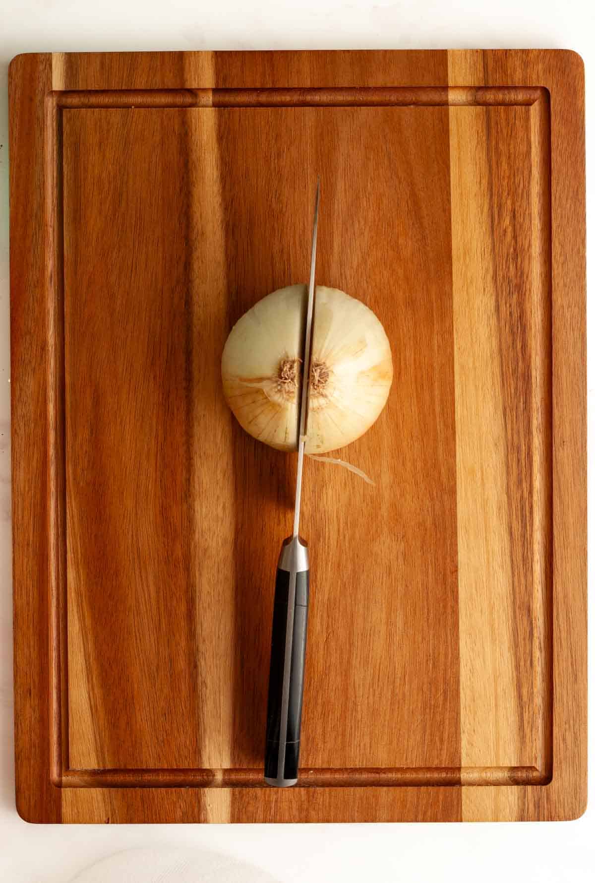 A knife cutting an onion in half on a wooden cutting board.
