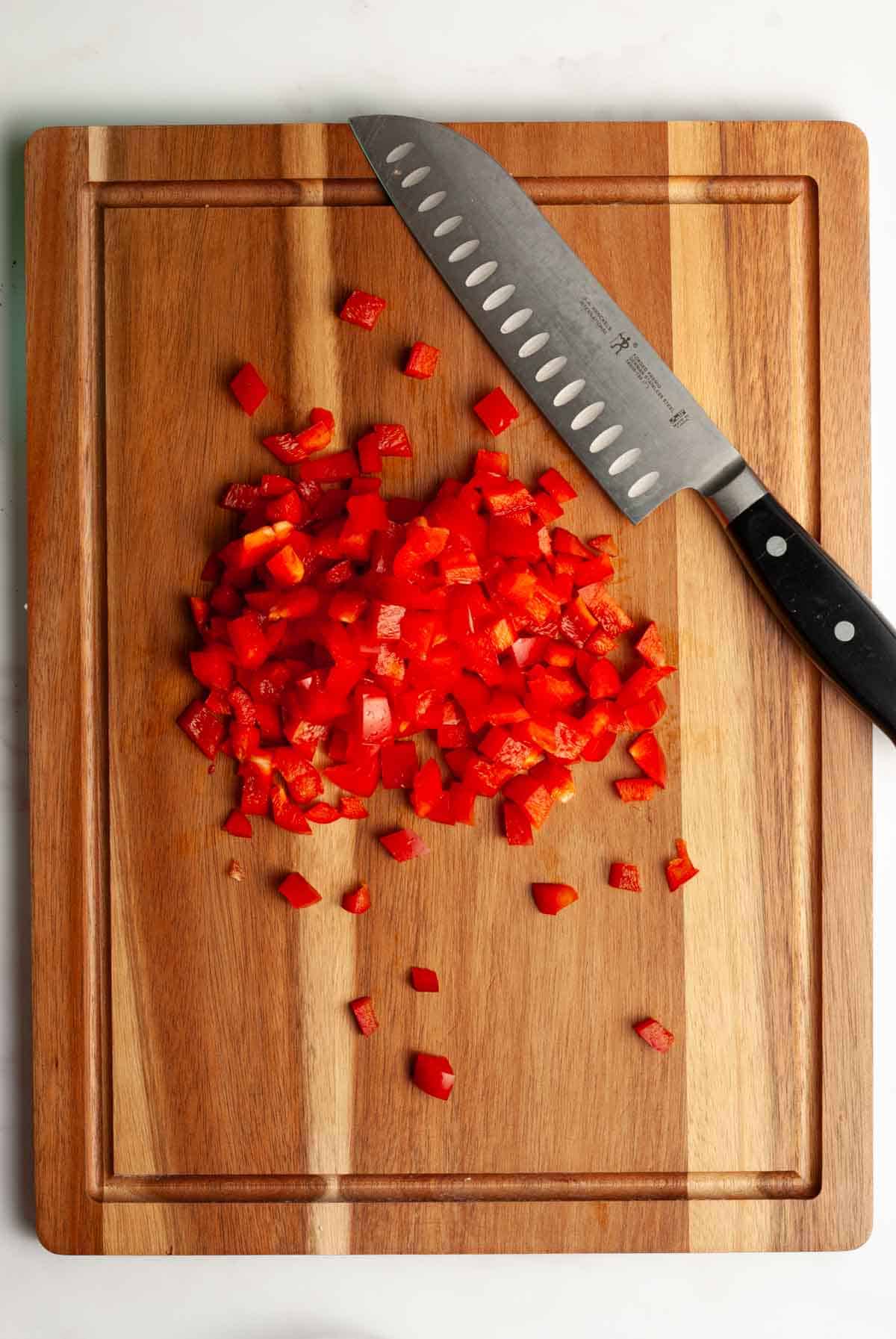 A pile of chopped red bell pepper on a wooden cutting board with a large chopping knife.