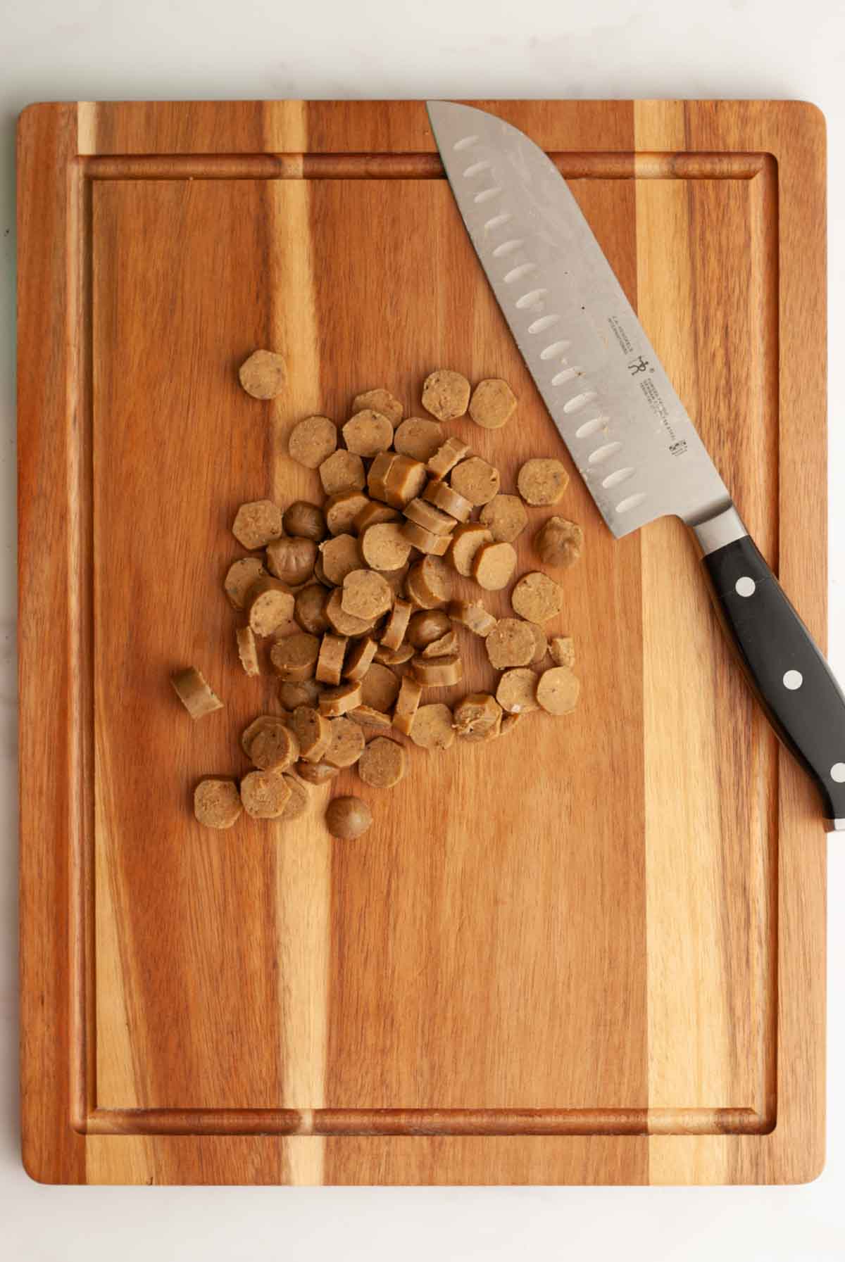 A pile of sliced vegan breakfast sausage links on a wooden cutting board with a large chopping knife.