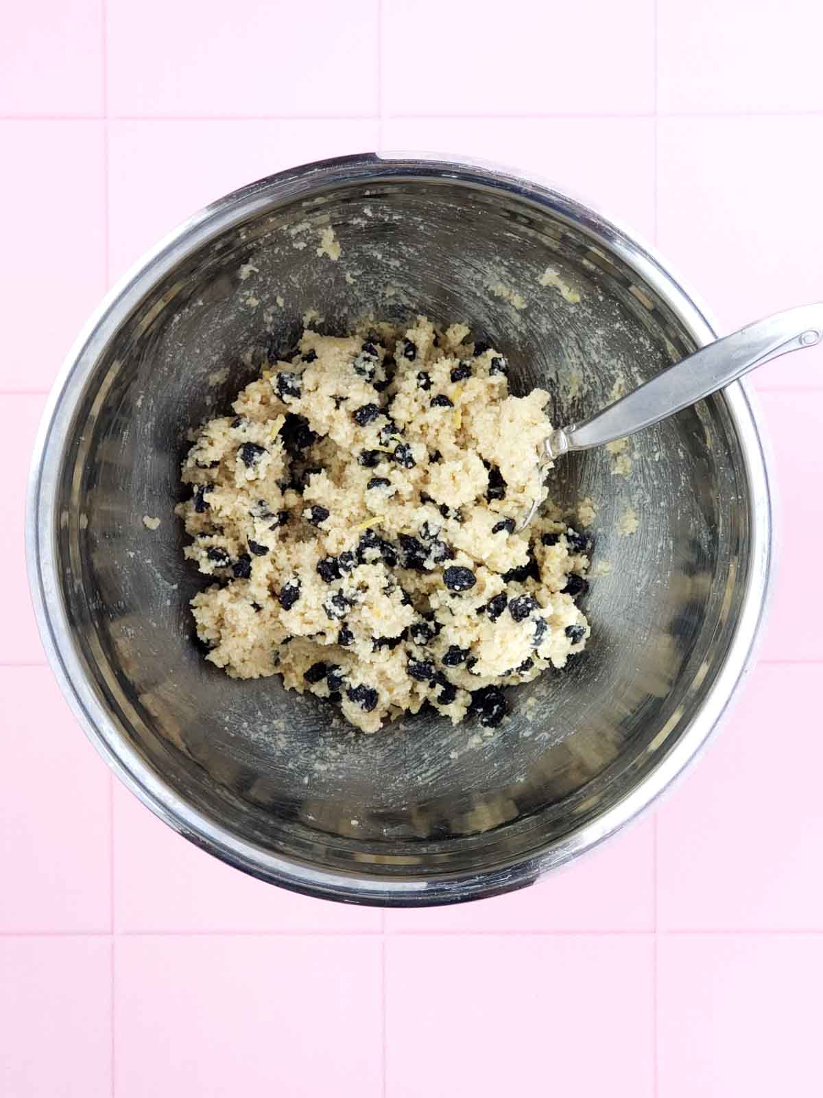 A mixing bowl and spoon showing all ingredients for the lemon blueberry cookies combined in the bowl.