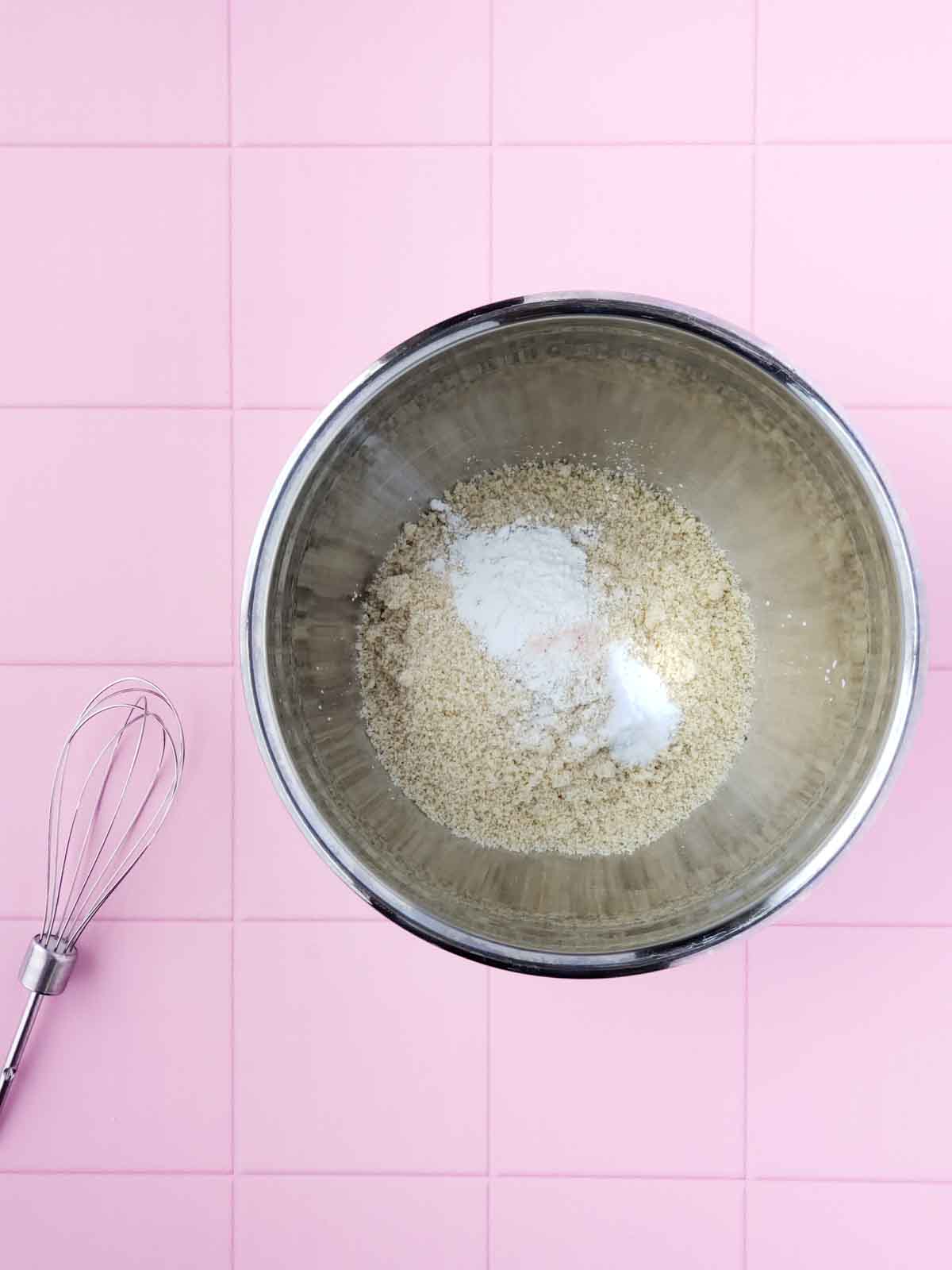All dry ingredients for the cookie recipe shown in a mixing bowl. A whisk is next to the bowl.