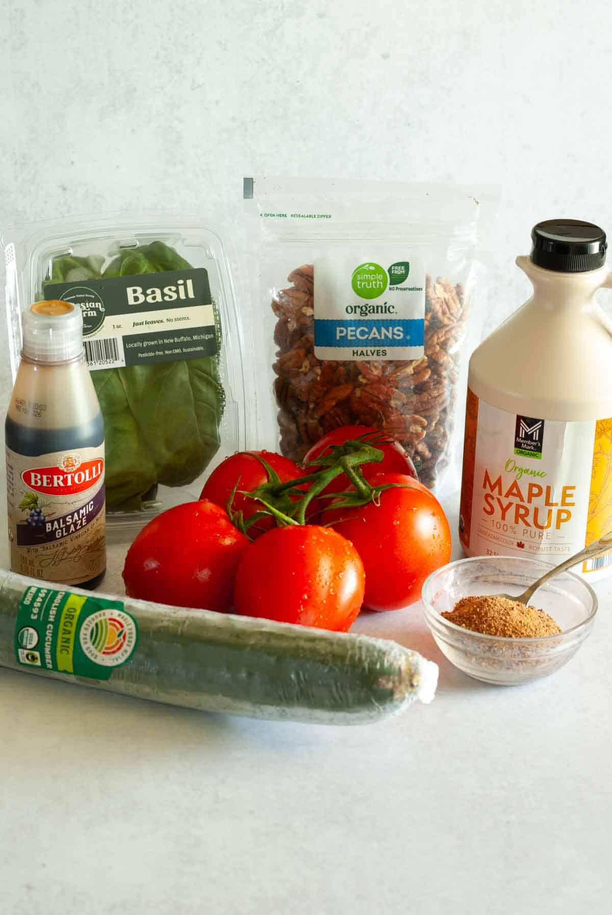 Ingredients for tomato, basil, cucumber salad including coconut sugar, syrup, basil leaves, tomatoes, pecans, and balsamic glaze.