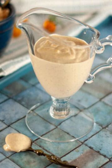 A small glass sauce boat filled with creamy vegan cashew based italian dressing. A small antique spoon with dressing on it.
