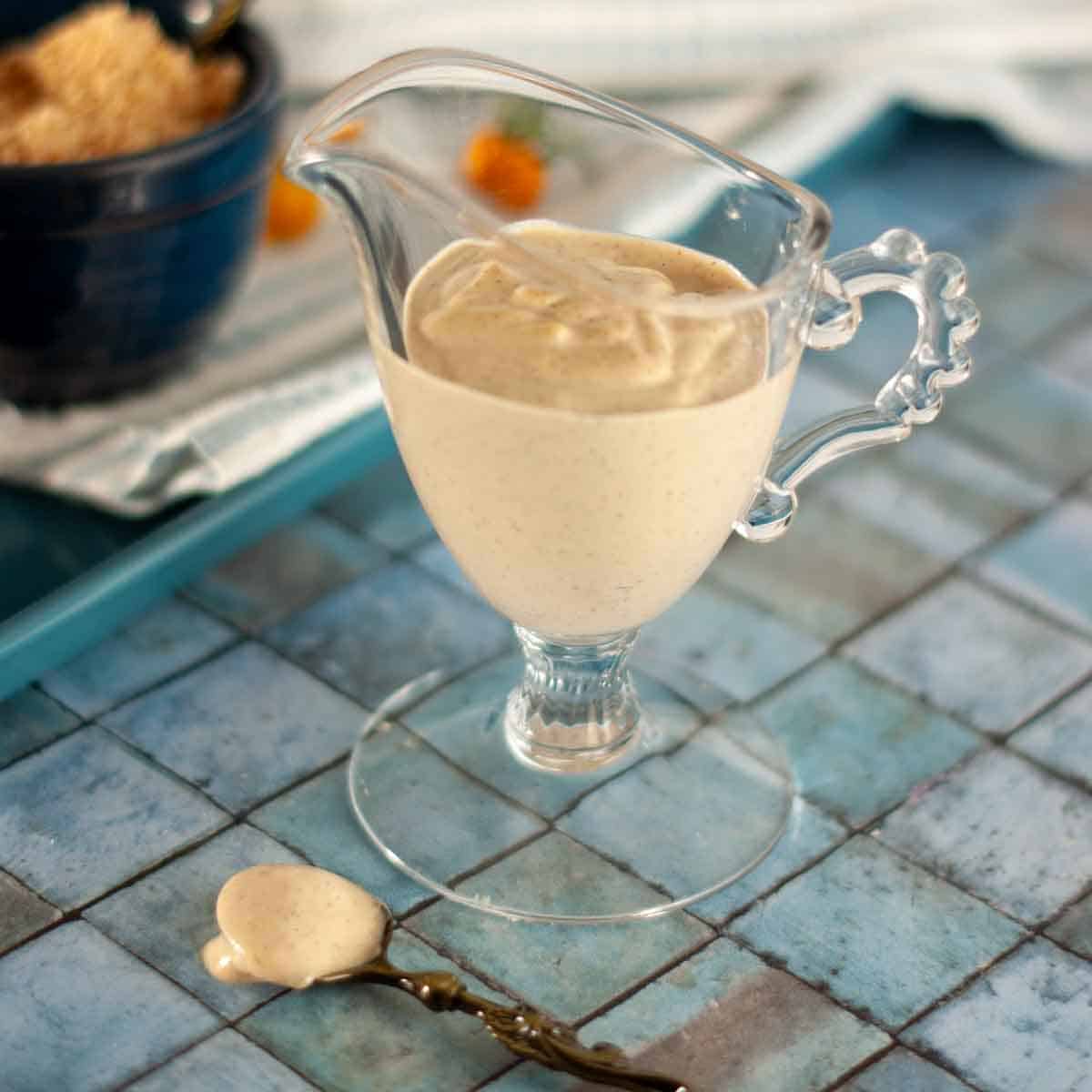 A small glass sauce boat filled with creamy vegan cashew based italian dressing. A small antique spoon with dressing on it.