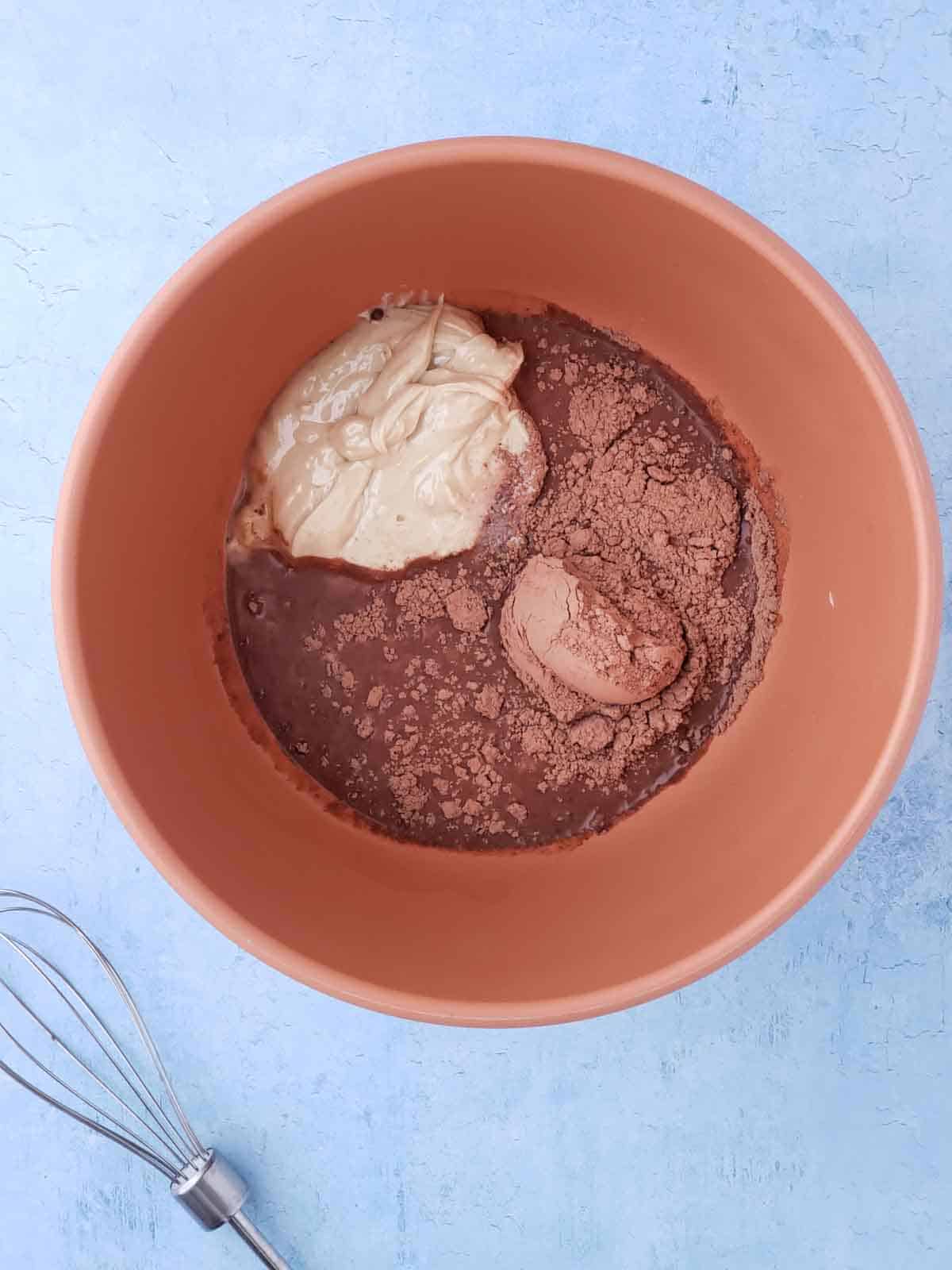 A mixing bowl with ingredients for making the chewy chocolate refrigerator cookies, including cashew butter, cocoa powder, and maple syrup.