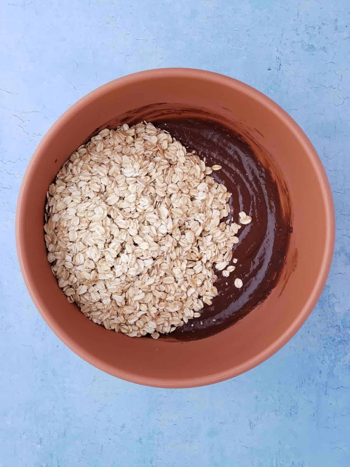 Raw oats being added to the mixing bowl of combined wet ingredients for the cookies.