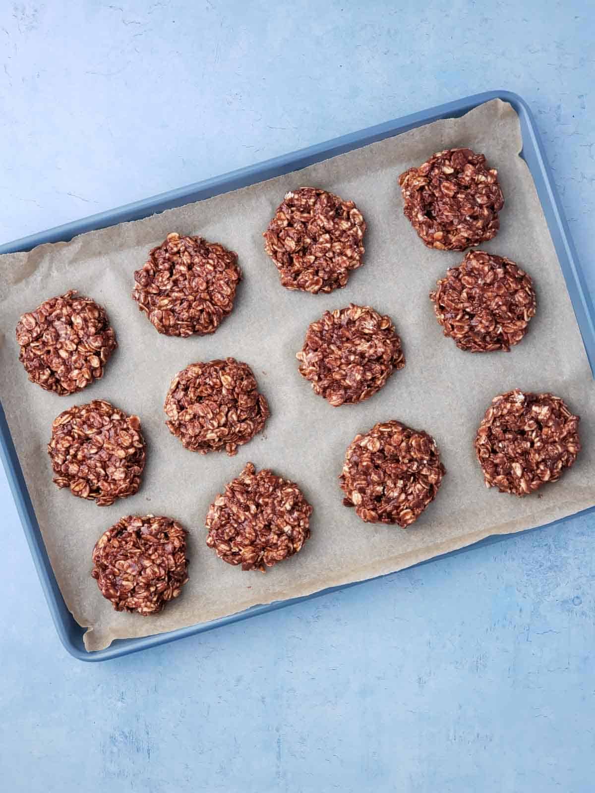 A blue cookie sheet lined with parchment and 12 cookies ready to go into the fridge to set up.