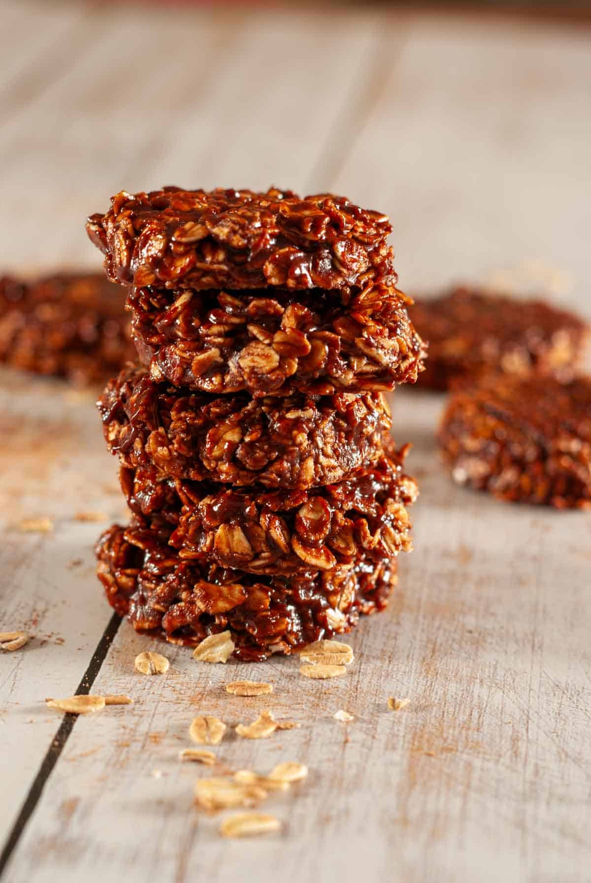 A stack of 5 chewy chocolate refrigerator cookies on a wooden table with some raw oats scattered about.