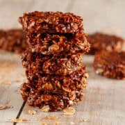 A stack of 5 chewy chocolate refrigerator cookies on a wooden table with some raw oats scattered about.