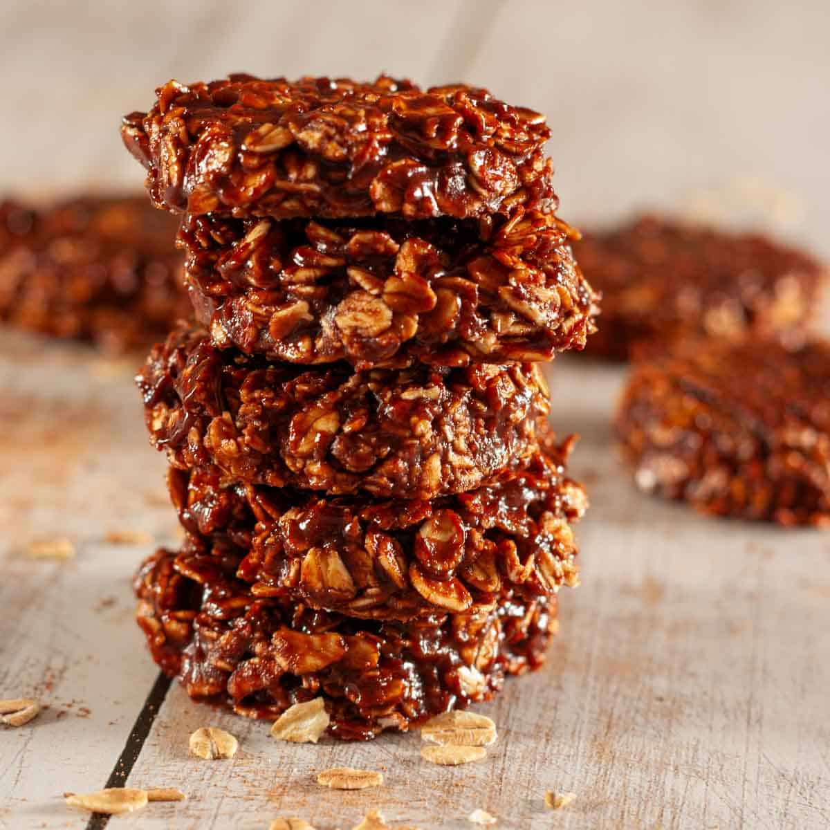 A stack of 5 chewy chocolate refrigerator cookies on a wooden table with some raw oats scattered about.