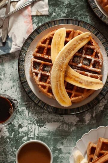 Close overhead shot of vegan oat buckwheat waffles topped with banana slices and powdered sugar.
