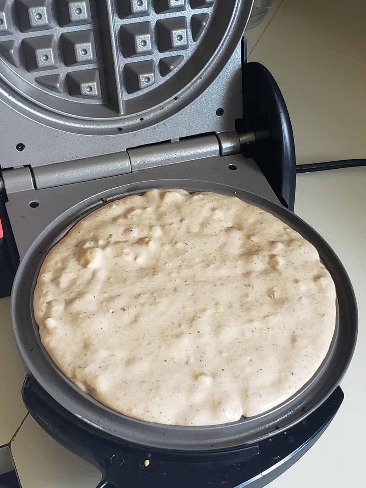 Waffle batter spread in round waffle maker before cooking.