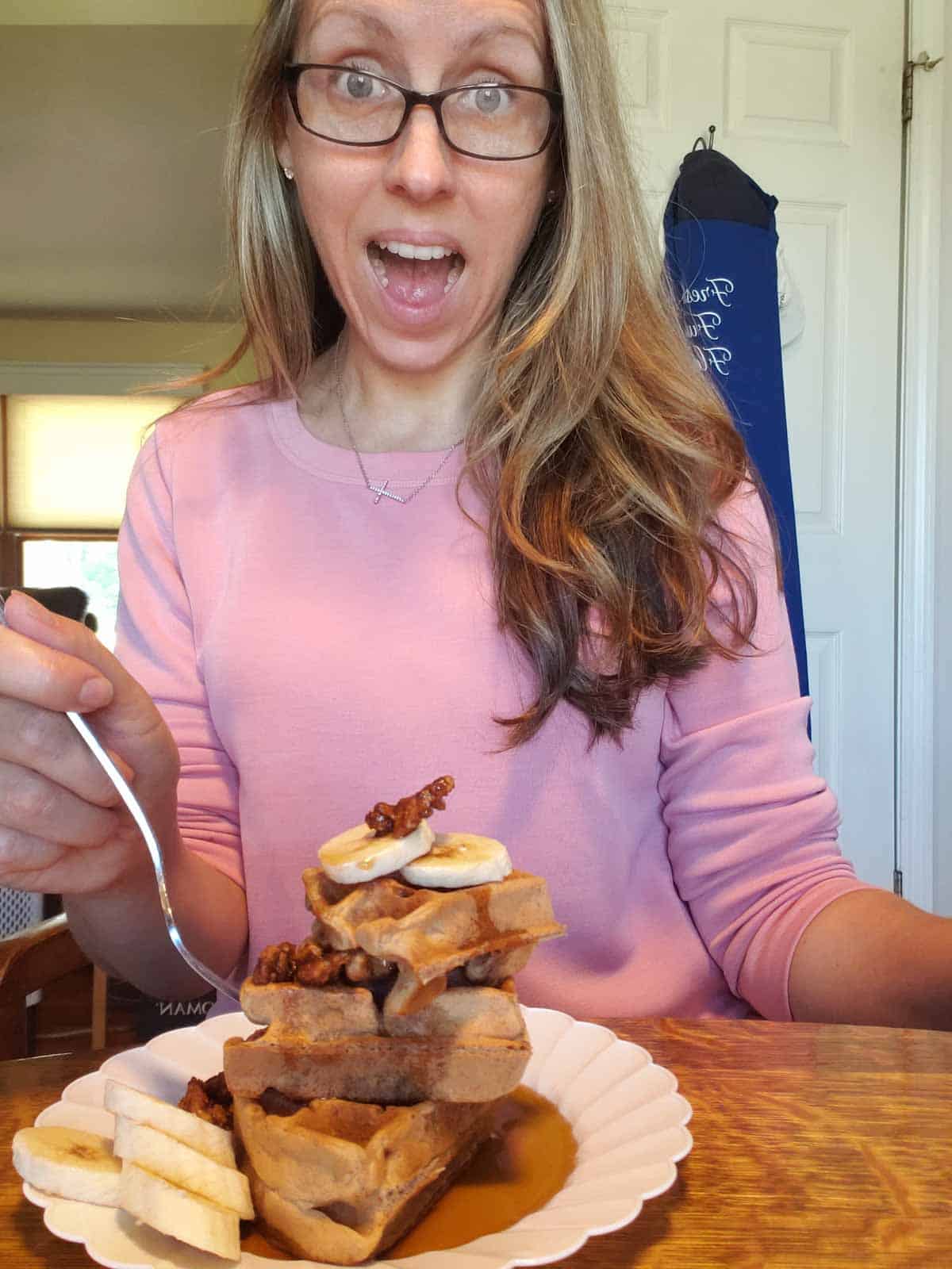 Rhonda smiling with plate of stacked vegan banana waffles topped with bananas and pecans.